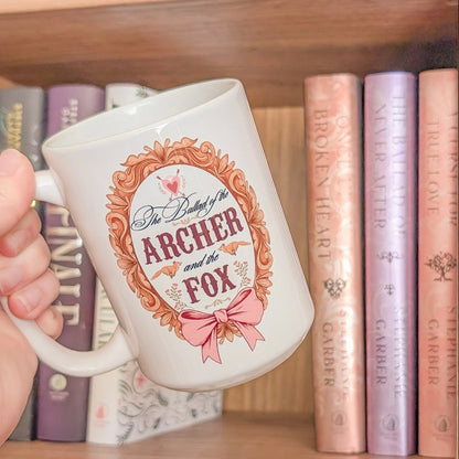 Mug with 'The Archer and the Fox' design held in front of a bookshelf with books.